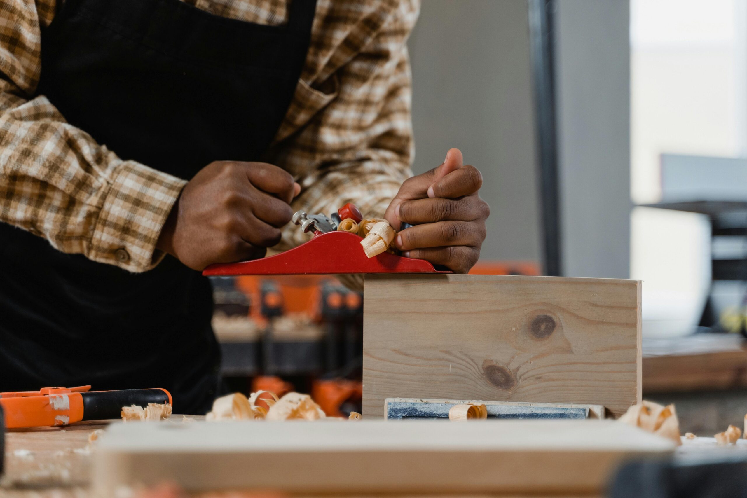 Close-up of a craftsman using a hand plane on wood in a workshop setting.